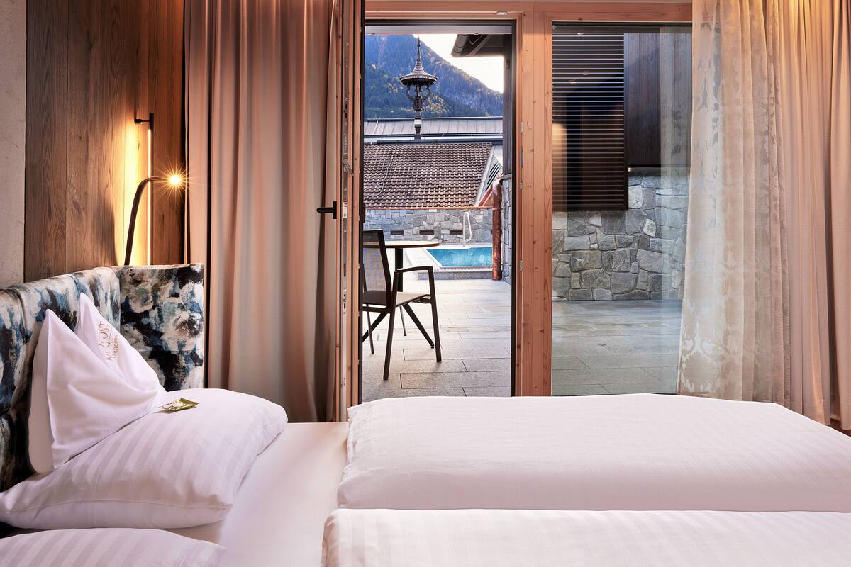 A bedroom with a large bed, a chair, and a view of an outdoor pool area.