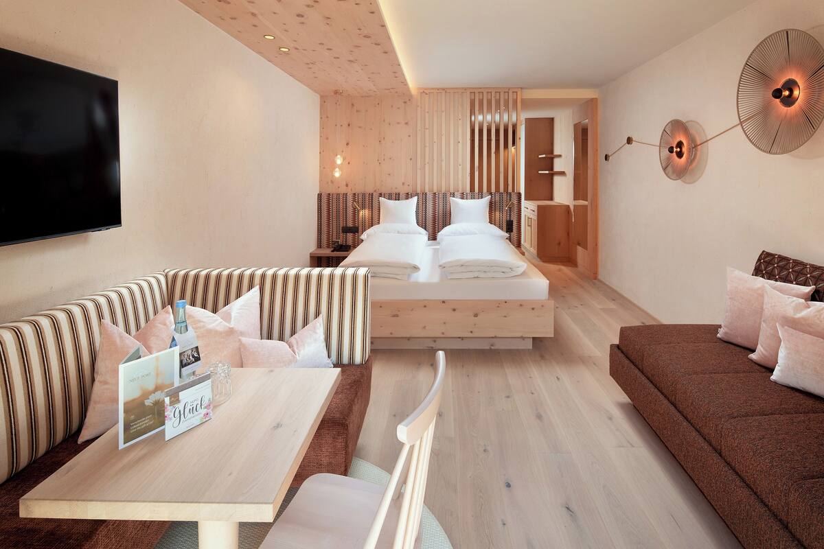 A modern hotel room with a large bed, a sofa, a dining table, and a TV.