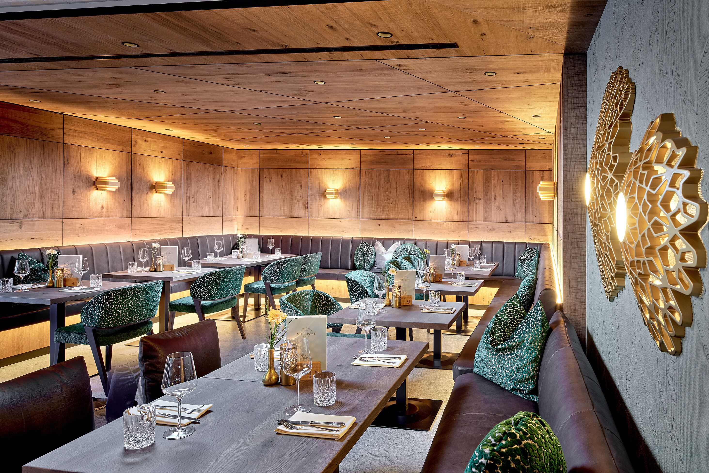 Un restaurante con paredes de paneles de madera, sillas tapizadas de verde y mesas dispuestas para comer.