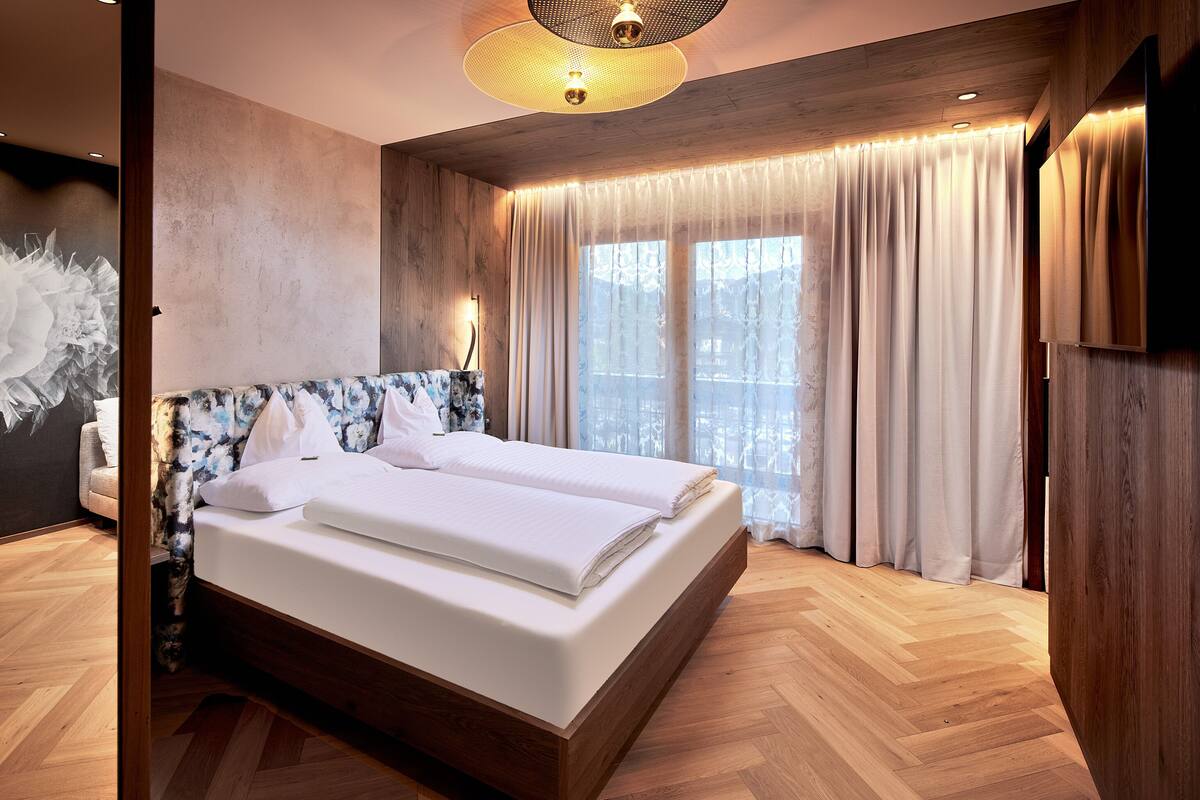 A modern bedroom with a large bed, wooden headboard, and a large window with curtains.