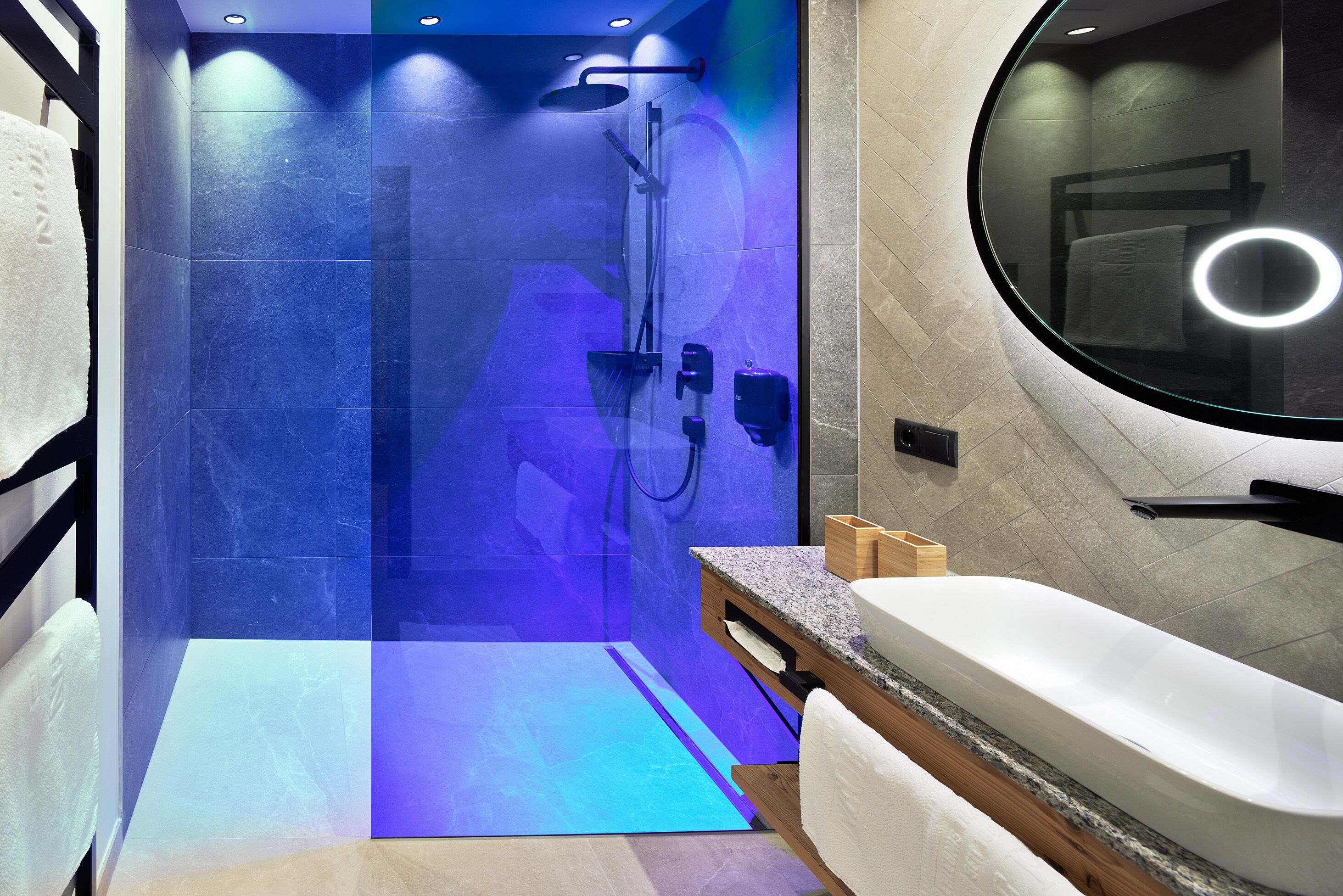 Un baño moderno con ducha envuelta en vidrio, tocador de madera y un espejo grande.