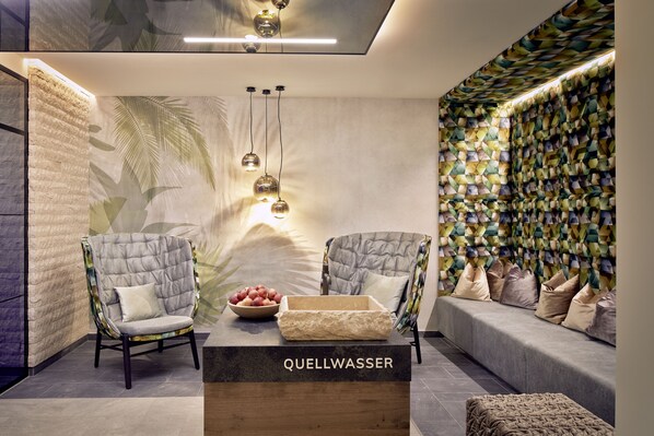 Un área de descanso moderna con dos sillones tapizados, una mesa de centro de madera y un muro con estampado.