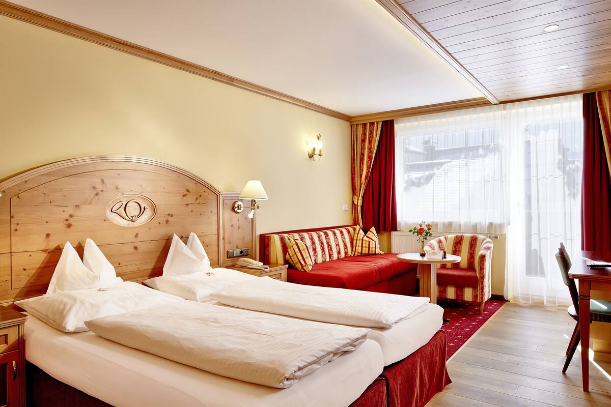 A hotel room with a wooden headboard, two beds with white linens, a red sofa, a small round table, and a chair.