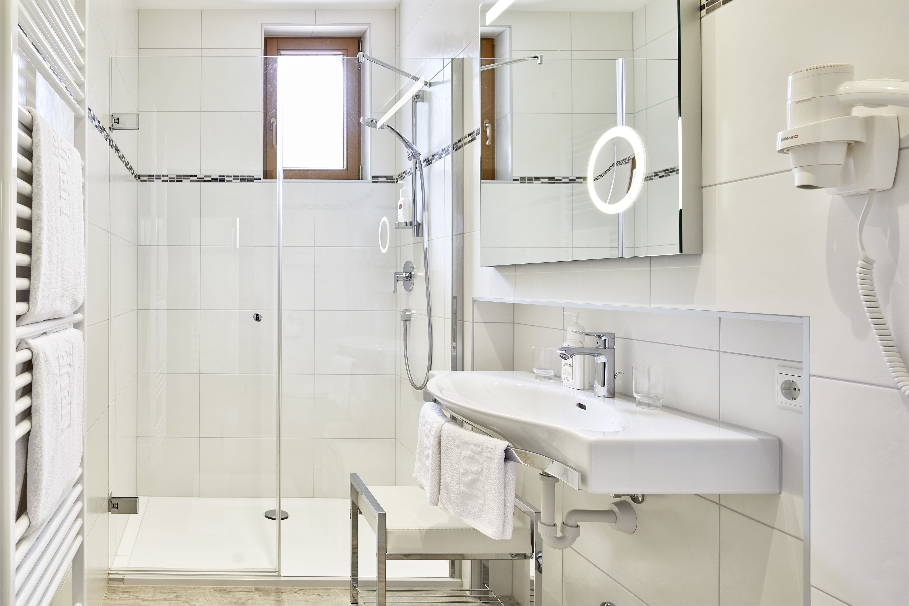 Ein modernes Badezimmer mit einer Duschkabine aus Glas, einem weißen Waschbecken und einem Spiegel mit integrierter Beleuchtung.