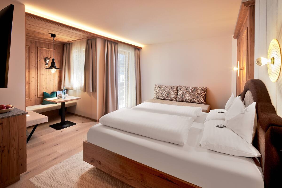 A modern hotel room with a wooden bed, a small desk, and a window with curtains.