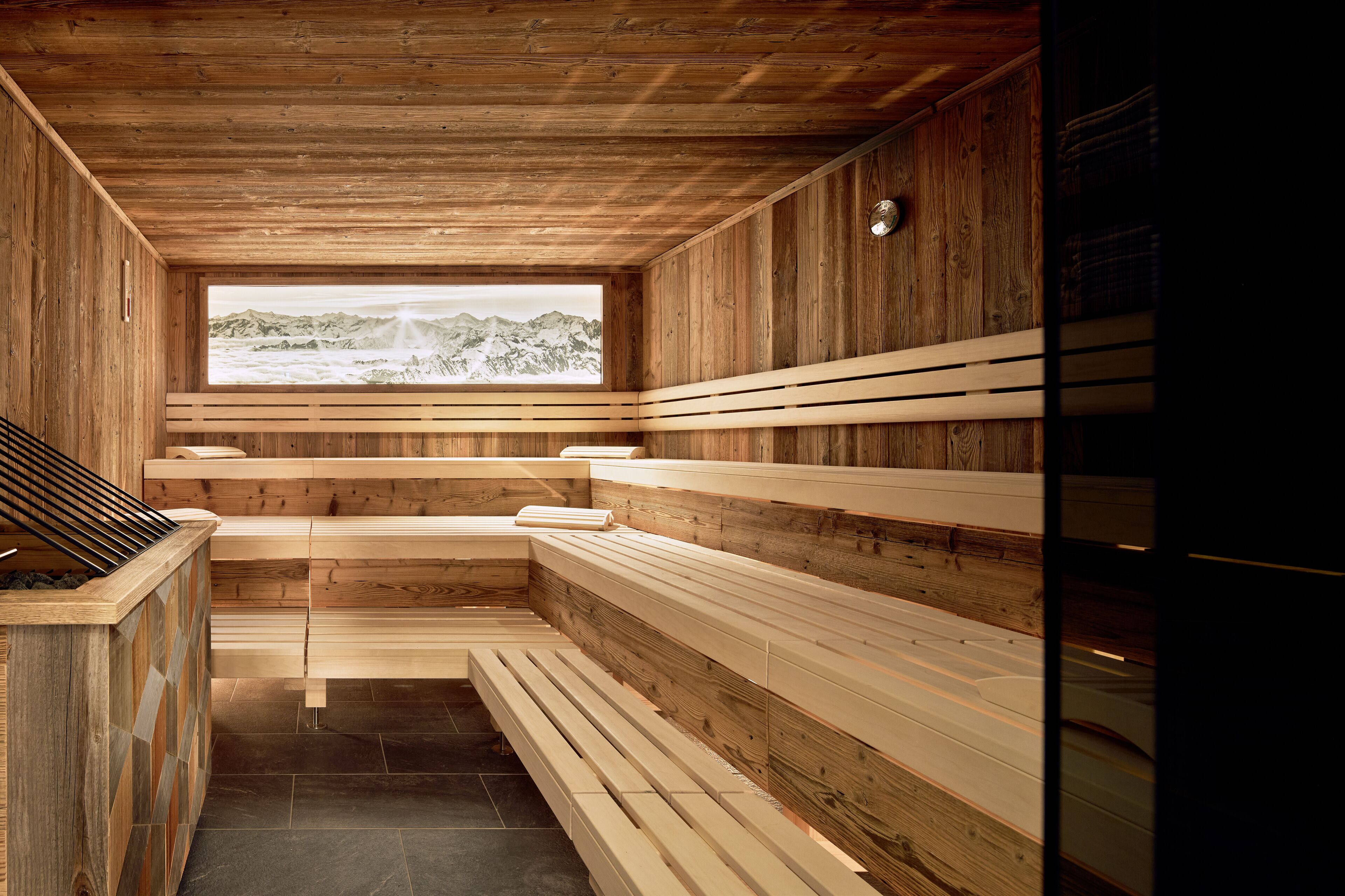 Un sauna avec des bancs en bois et une vue sur les montagnes, visible à travers une grande fenêtre.