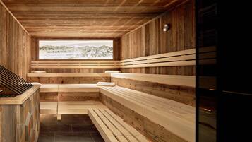 Un sauna avec des bancs en bois et une vue sur les montagnes, visible à travers une grande fenêtre.