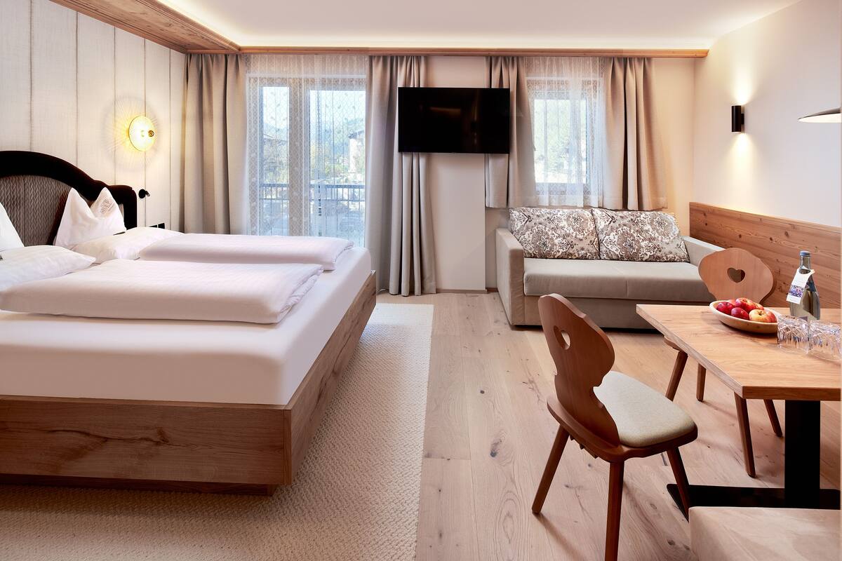 A hotel room with a bed, a sofa, a TV, and a dining area with a table and chairs.
