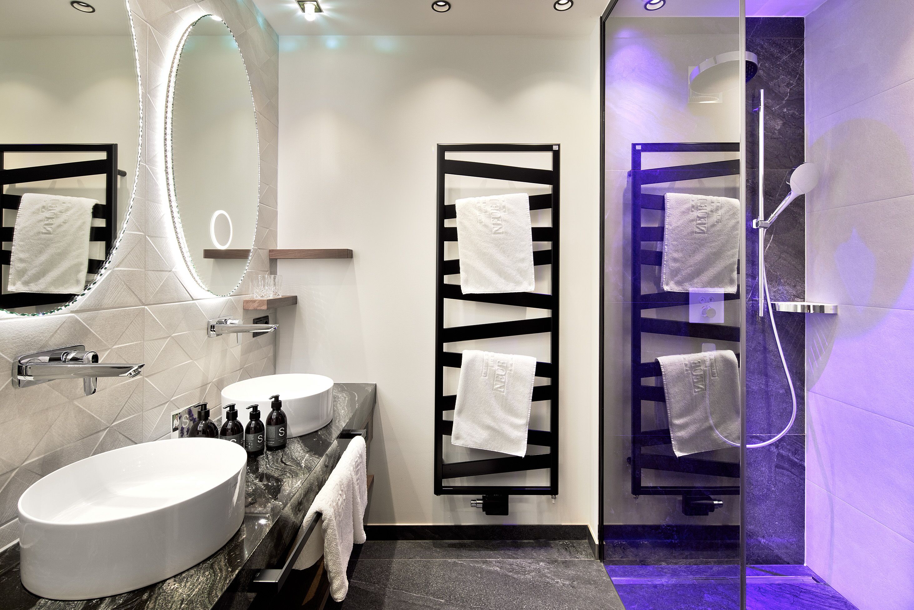 A modern bathroom with a large oval sink, a mirror with LED lights, and a glass-enclosed shower area.