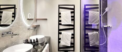 A modern bathroom with a large oval sink, a mirror with LED lights, and a glass-enclosed shower area.