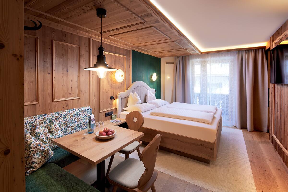 A wooden room with a bed, a table with a bowl of fruit, and a bench.