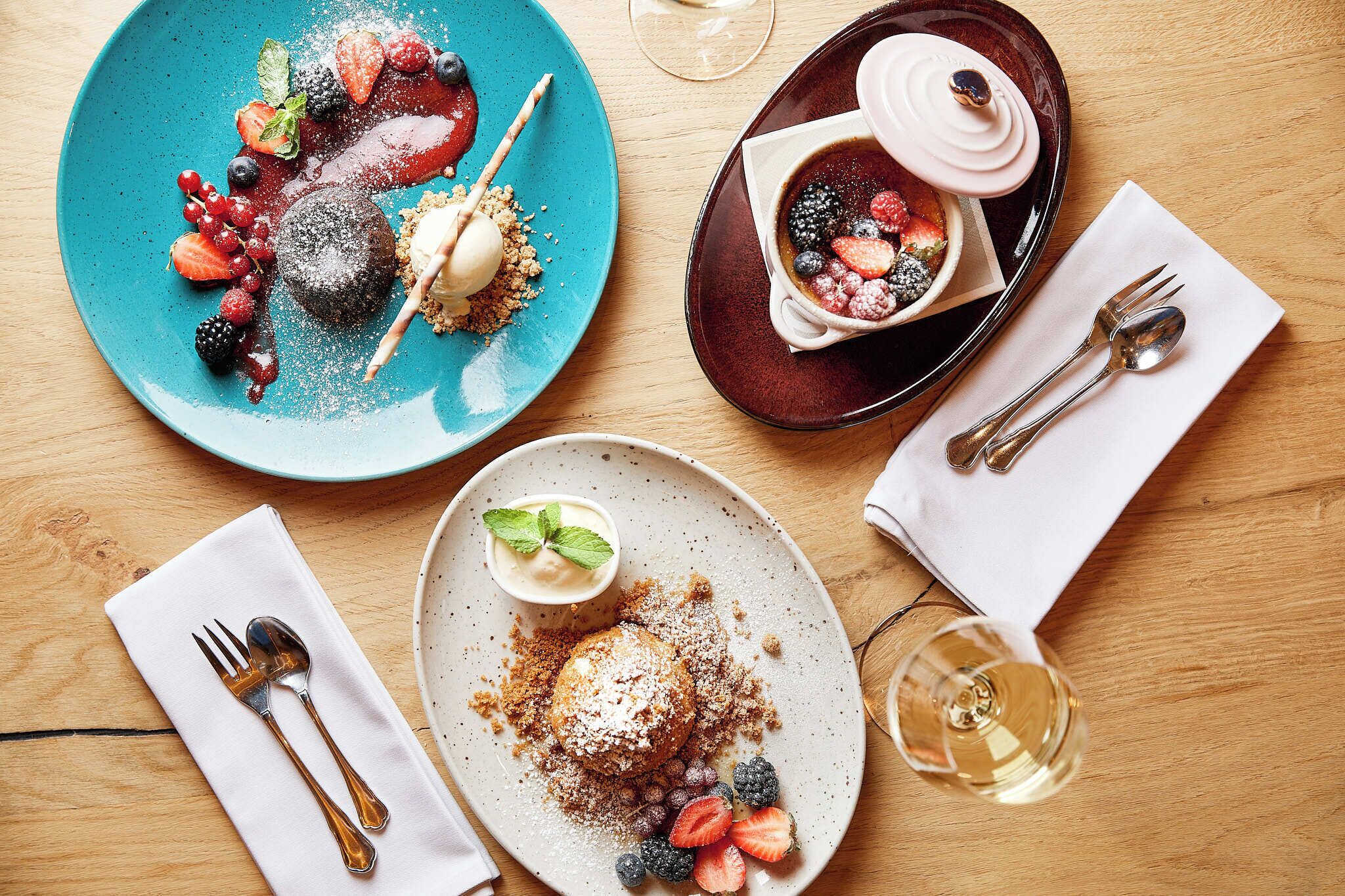 A table set with various desserts, a glass of wine, and neatly arranged cutlery.