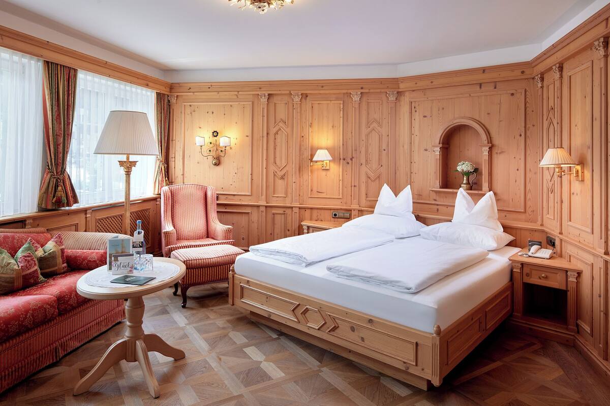 A hotel room with a large bed, a red sofa, a wooden floor, and a chandelier.
