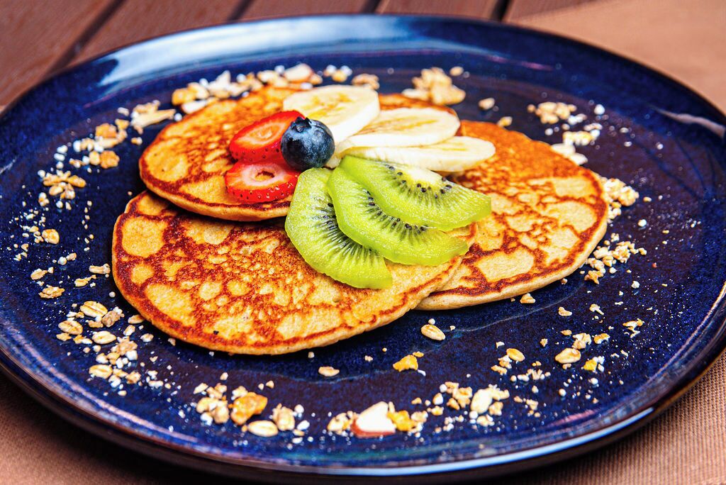 Une assiette de crêpes garnie de tranches de bananes, de kiwis, de myrtilles et de fraises, et saupoudrée de granola.