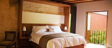 Un dormitorio con una cama grande, vigas de madera, pared de ladrillo y un balcón con vistas.