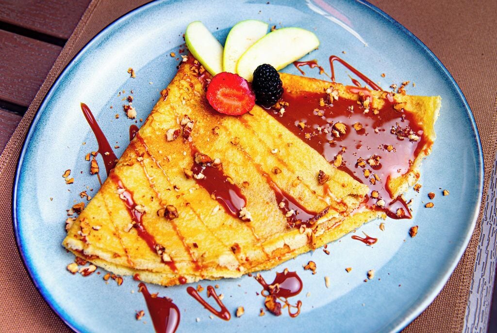 Una crepe con fruta y salsa sobre un plato.