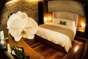 A hotel room with a large bed, two bedside lamps, a stone wall, and a potted orchid. - Casa Madero Hotel Boutique (Morelia)