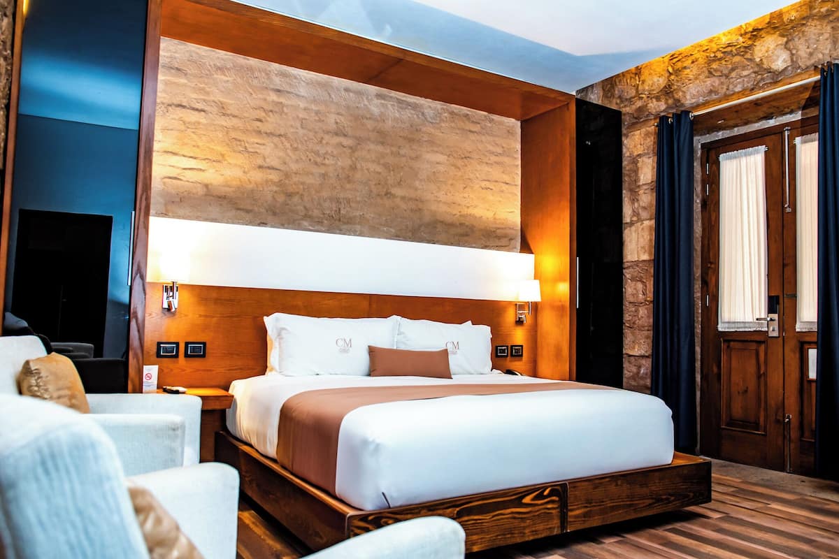 A modern hotel room with a large bed, wooden headboard, and stone accent wall.