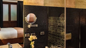A modern bathroom with a large mirror, a sink, and a toilet. There is a shower area with a glass door and a decorative wall.