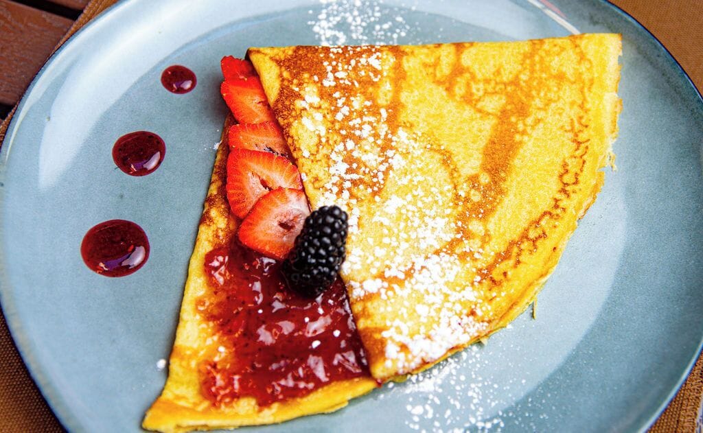 Crepe con fresas, zarzamoras y salsa de frutos rojos sobre un plato.