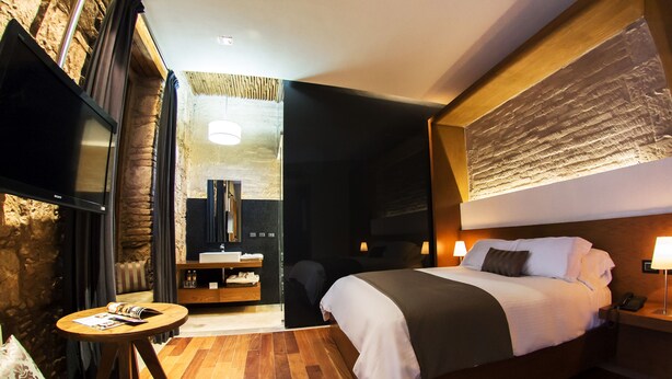 A modern hotel room with a large bed, a television, a small table, and a cozy seating area. - Casa Madero Hotel Boutique (Morelia)