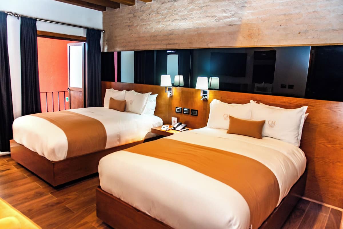 A hotel room with two beds, wooden headboards, and a brick wall.