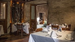 A restaurant with wooden tables and chairs, a wine rack, and a rustic brick wall. - Casa Madero Hotel Boutique (Morelia)