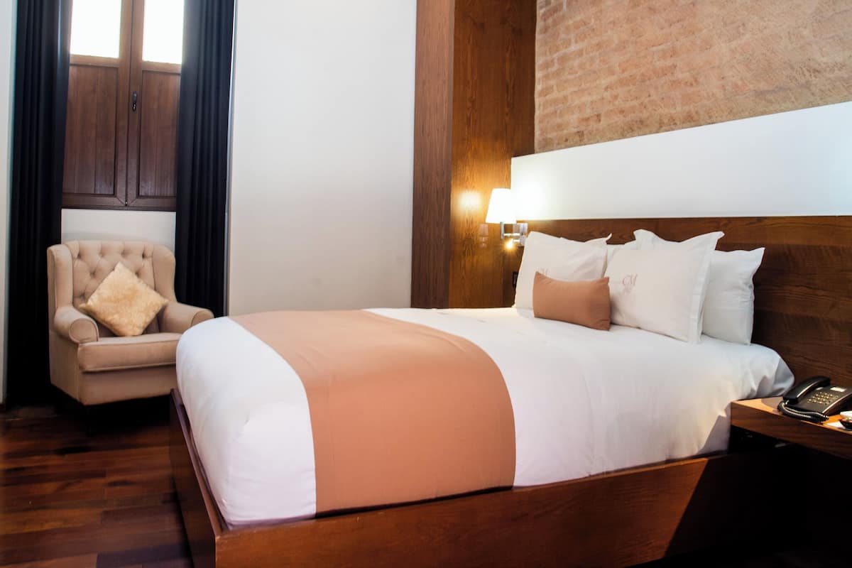 A hotel room with a large bed, a chair, a lamp, and a phone on the nightstand.