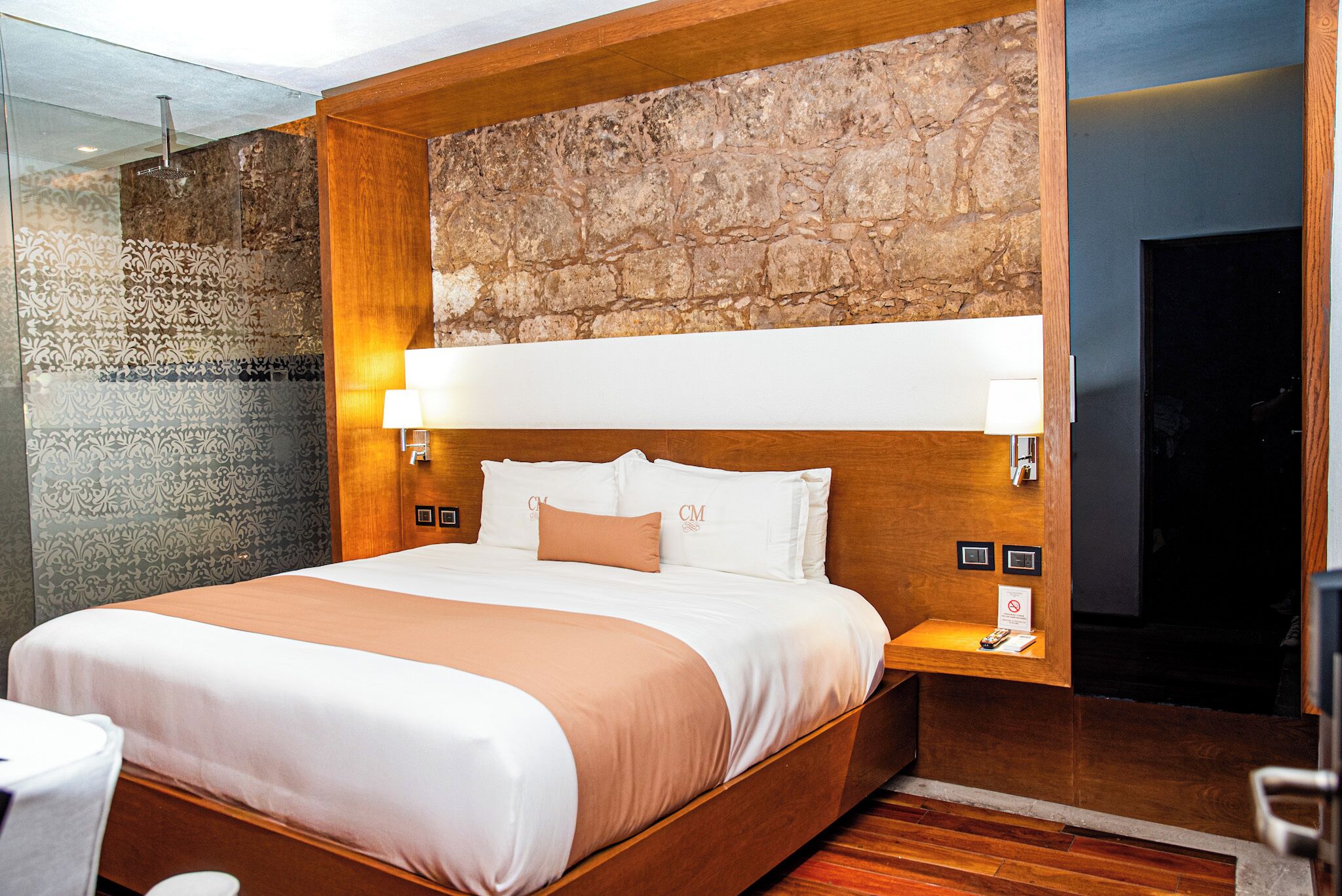 A hotel room with a large bed, a stone accent wall, and a wooden headboard.