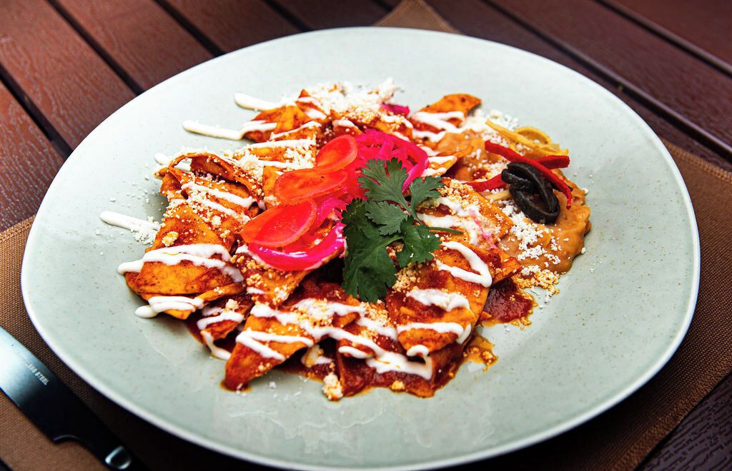 A plate of nachos with toppings and a knife on the side.