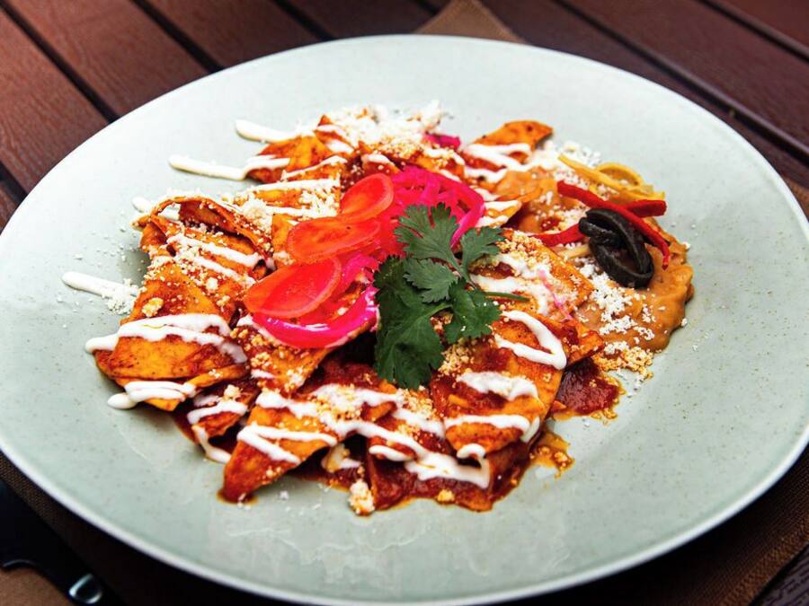 A plate of nachos with toppings and a knife on the side.