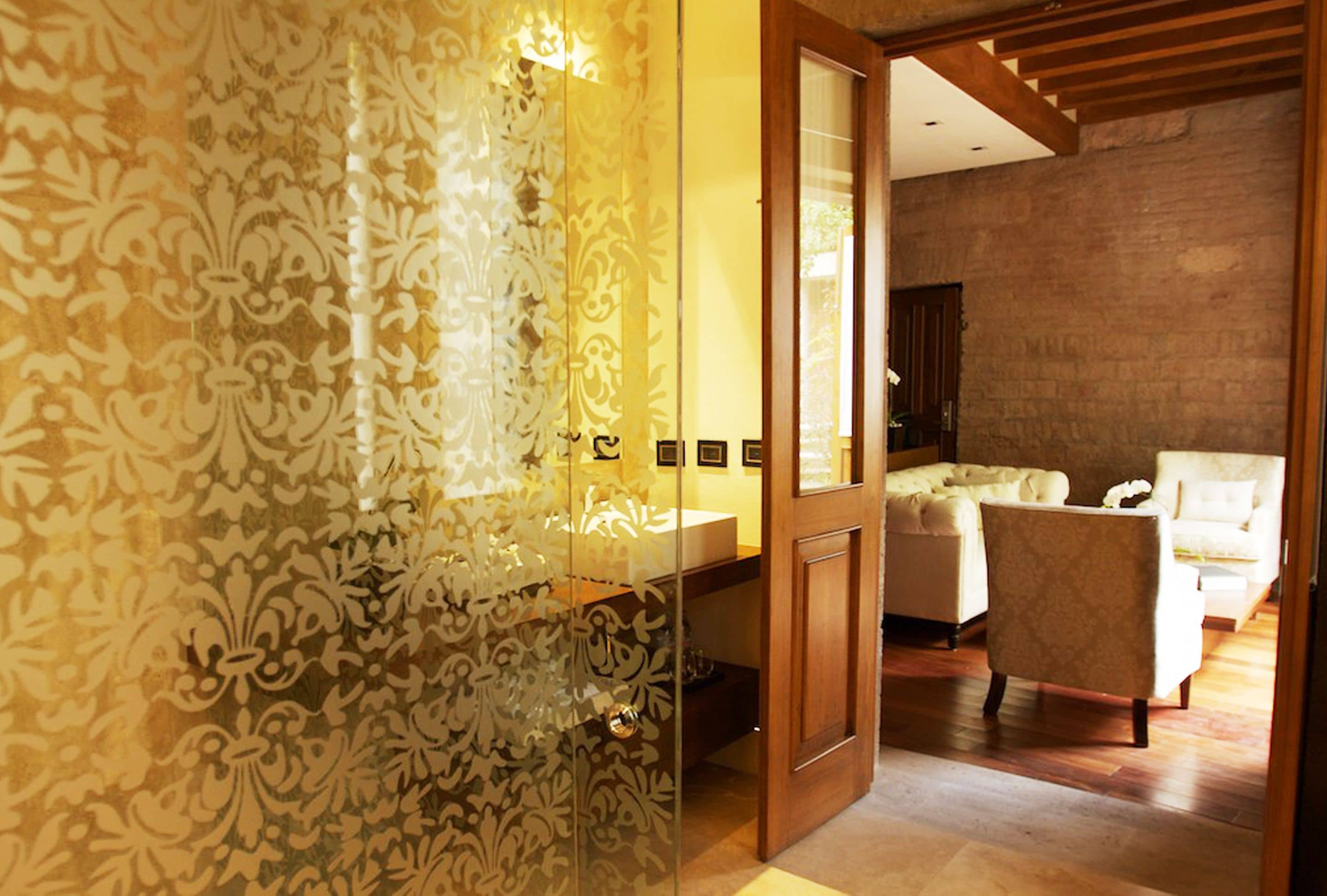 A modern bathroom with a glass shower enclosure and a wooden door leading to a bedroom with a bed and a chair.