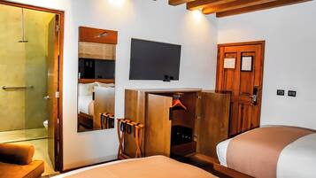 A hotel room with a bed, a TV mounted on the wall, a wooden wardrobe, a mirror, and a shower area.