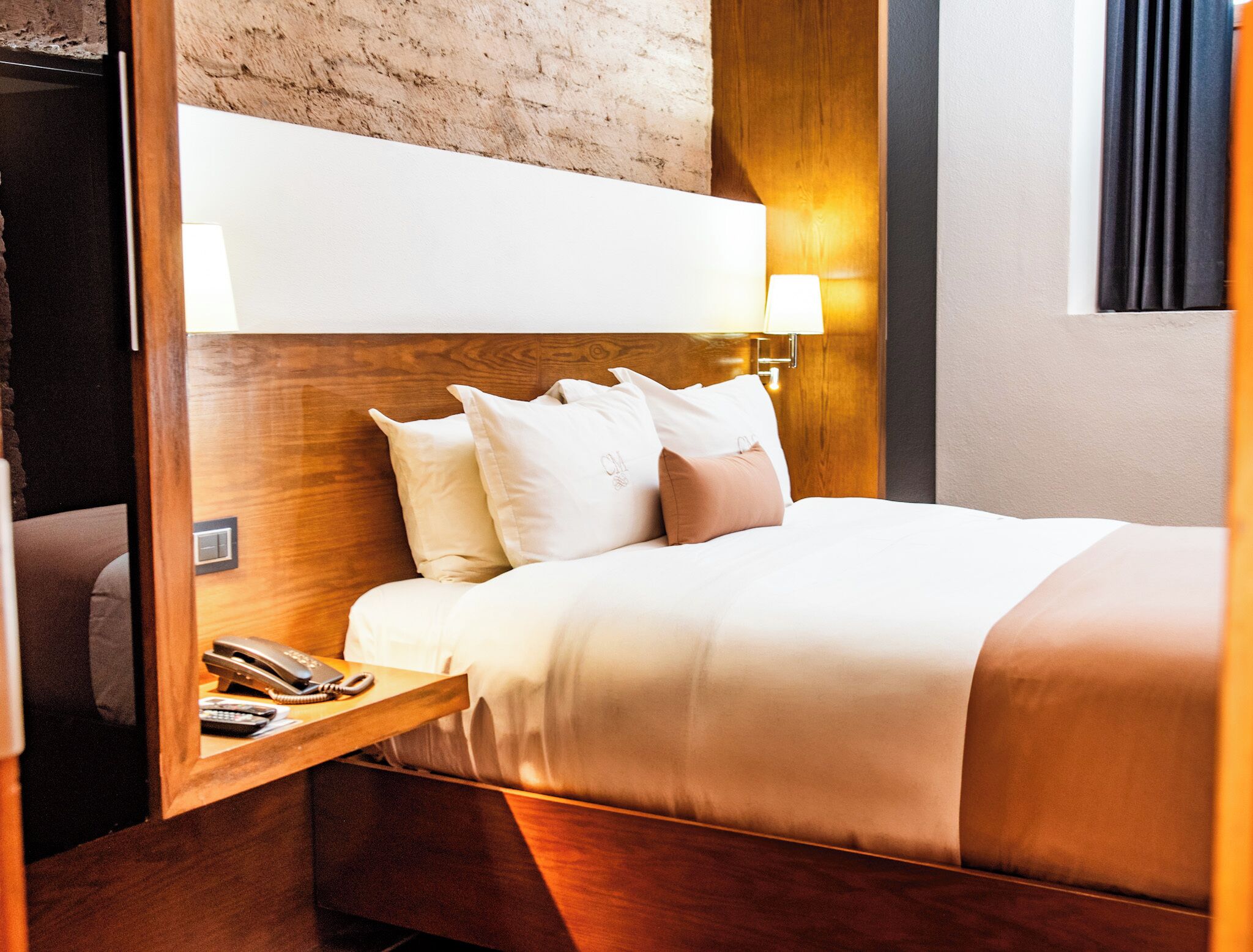A neatly made bed with a wooden headboard, a bedside table with a lamp, and a telephone.