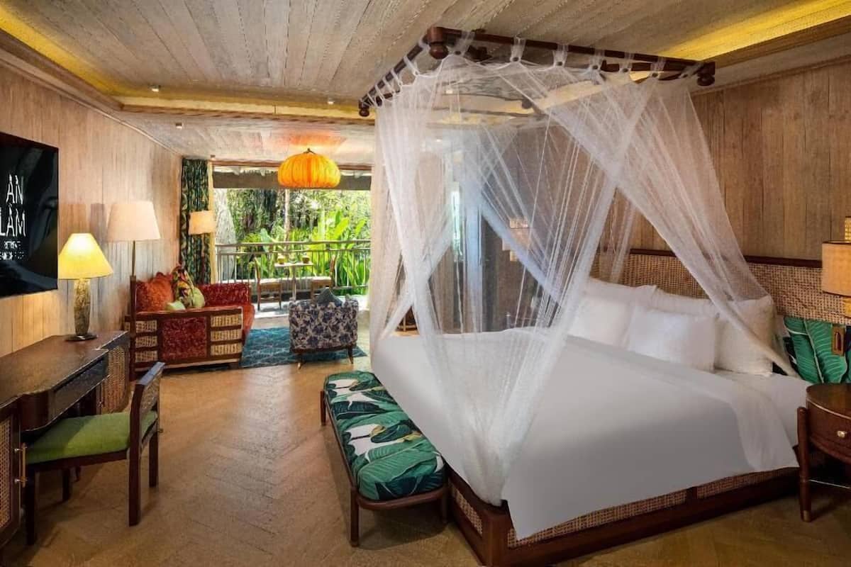 A room with a bed, a sofa, a bench, a table, and a TV.