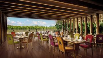Un área de comedor al aire libre con mesas de madera y sillas coloridas, con vistas a un paisaje verde exuberante.