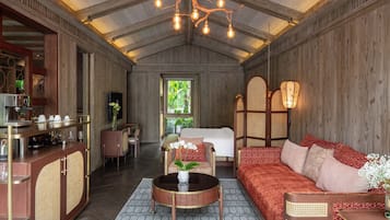 A spacious room with a high ceiling, a wooden ceiling, a dining area with a bar, a sofa set, and a bed with a view of greenery outside.
