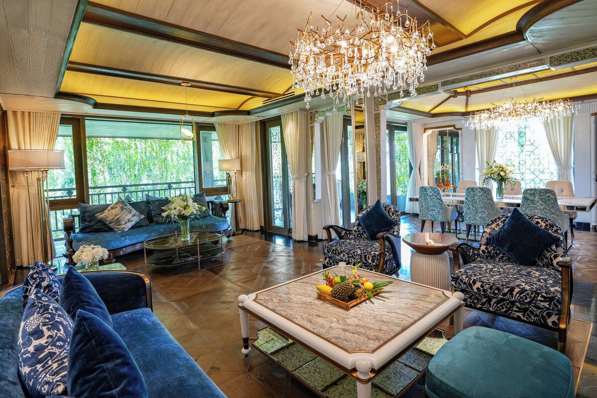 A spacious living room with a chandelier, blue sofas, and a dining area with chairs.