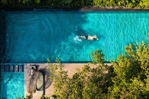 An aerial view of a swimming pool with a person swimming, surrounded by greenery and a wooden deck with lounge chairs. - An Lam Retreats Saigon River (Ho Chi Minh City)