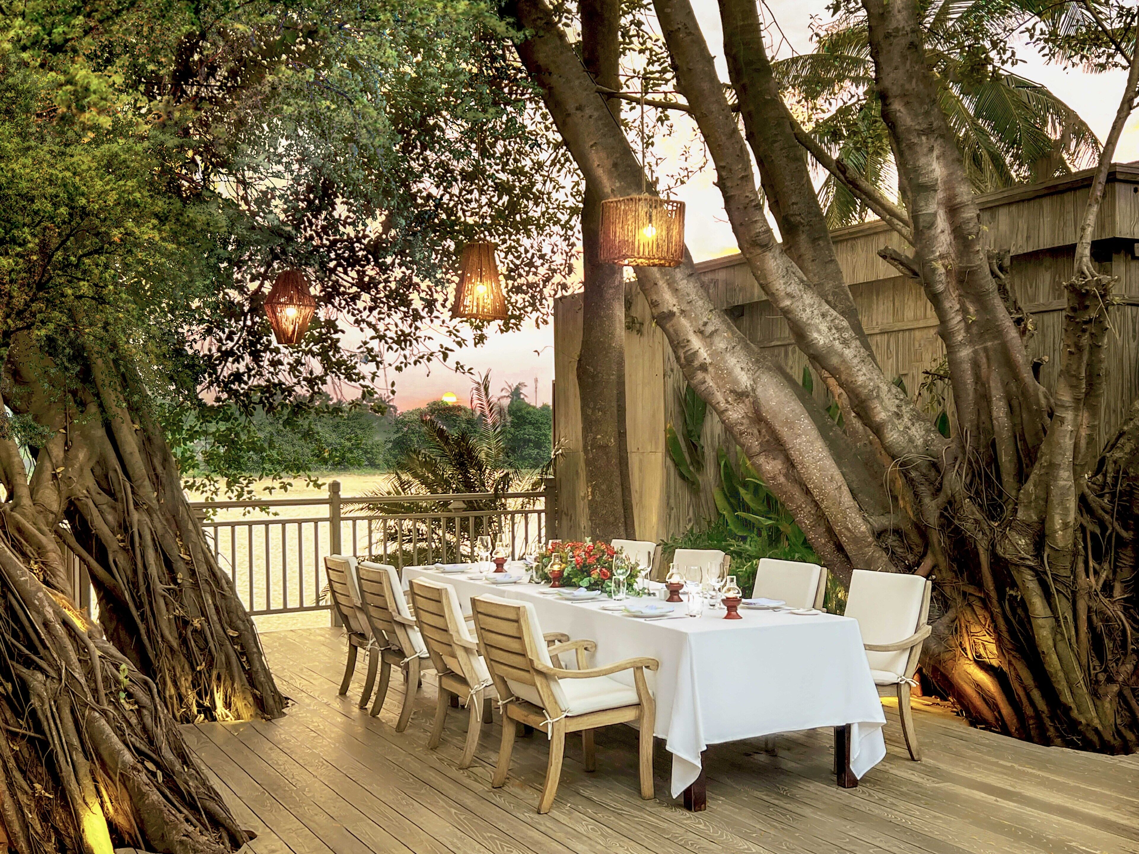 An outdoor dining area with a wooden deck, tables set for four, and hanging lanterns.