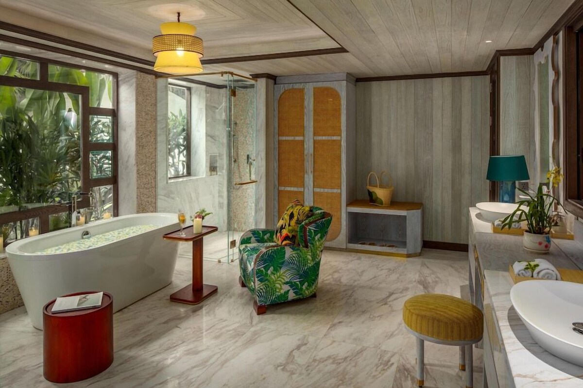 Une salle de bain avec une grande baignoire, une douche, un lavabo, une chaise et une petite table.