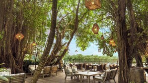An outdoor seating area with wooden tables and chairs, surrounded by large trees and hanging lanterns. - An Lam Retreats Saigon River (Ho Chi Minh City)