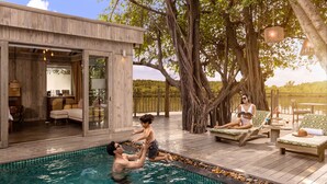 A pool area with a wooden deck, lounge chairs, and a large tree. - An Lam Retreats Saigon River (Ho Chi Minh City)