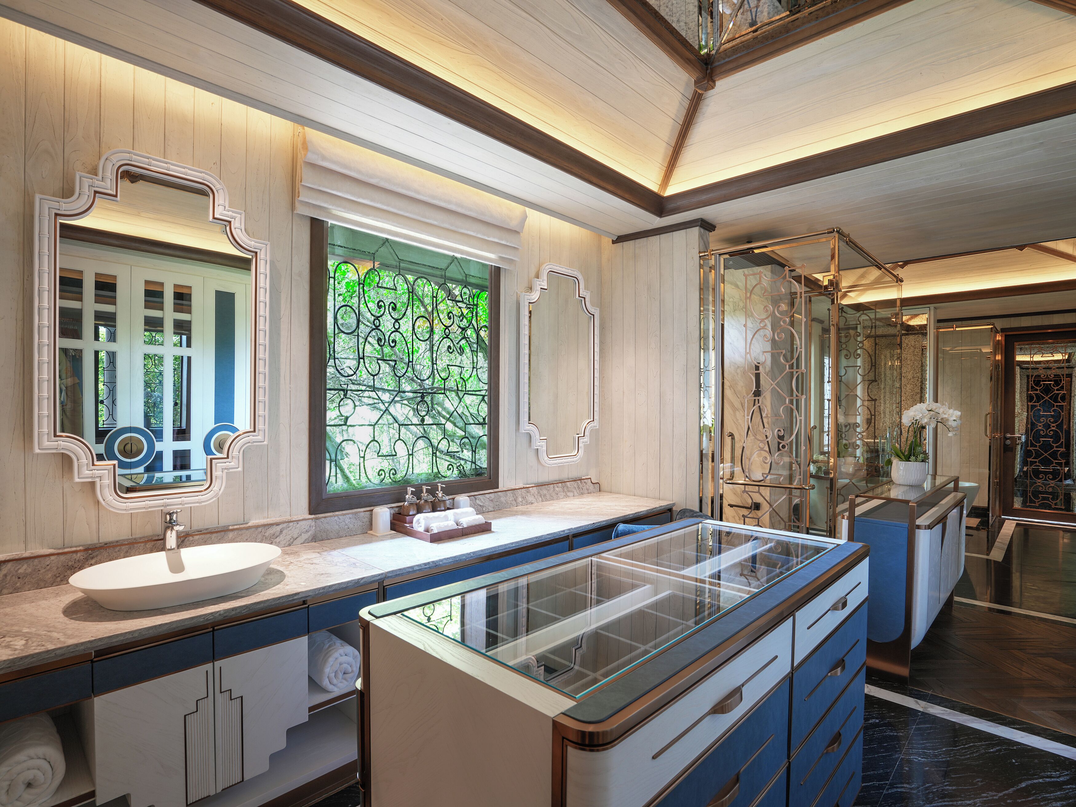 A modern bathroom with a large glass-enclosed shower, a white sink, and a decorative mirror.