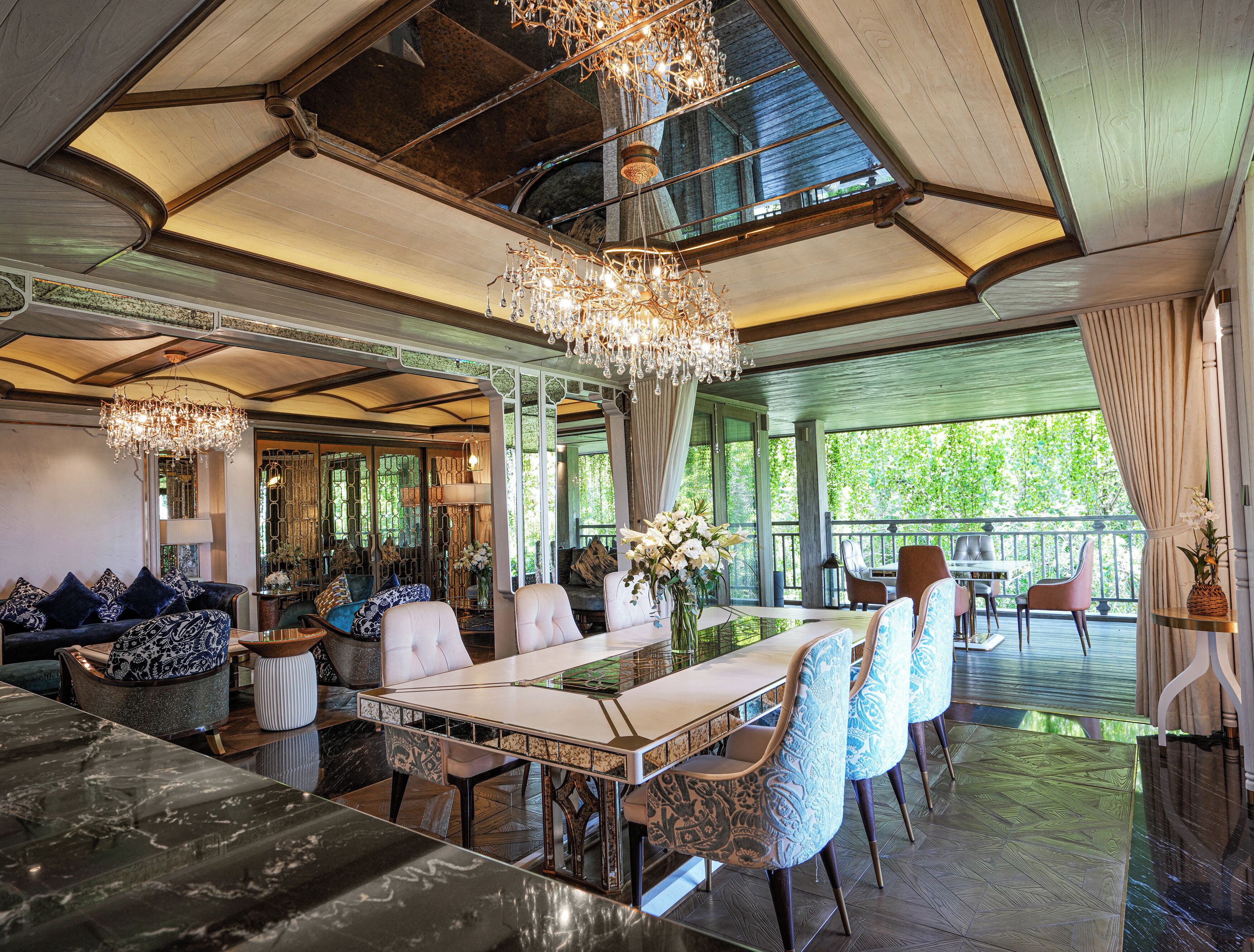 A spacious, elegantly furnished room with a high ceiling, large windows, and a chandelier.