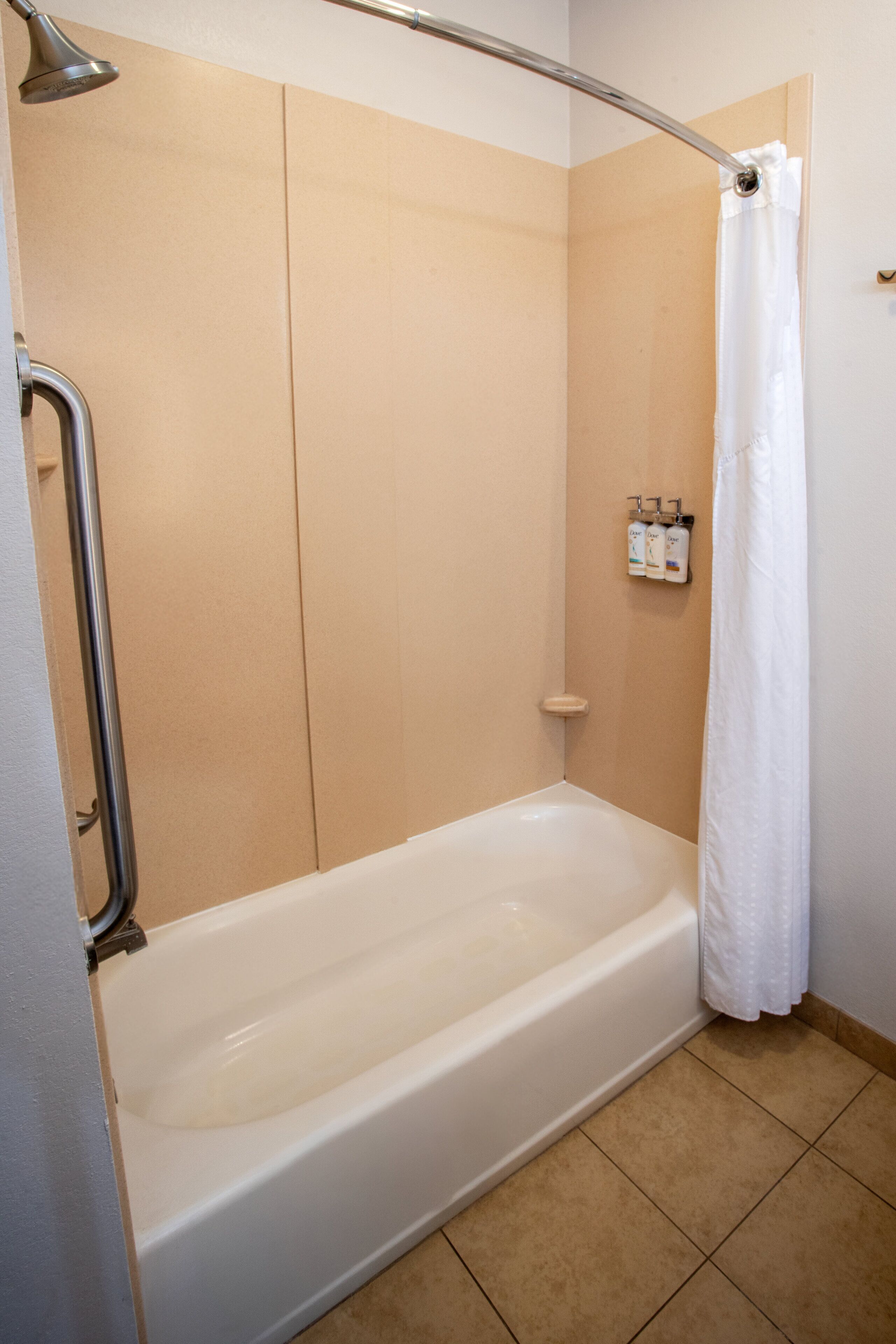 A standard hotel bathroom with a bathtub, shower, and a handrail.