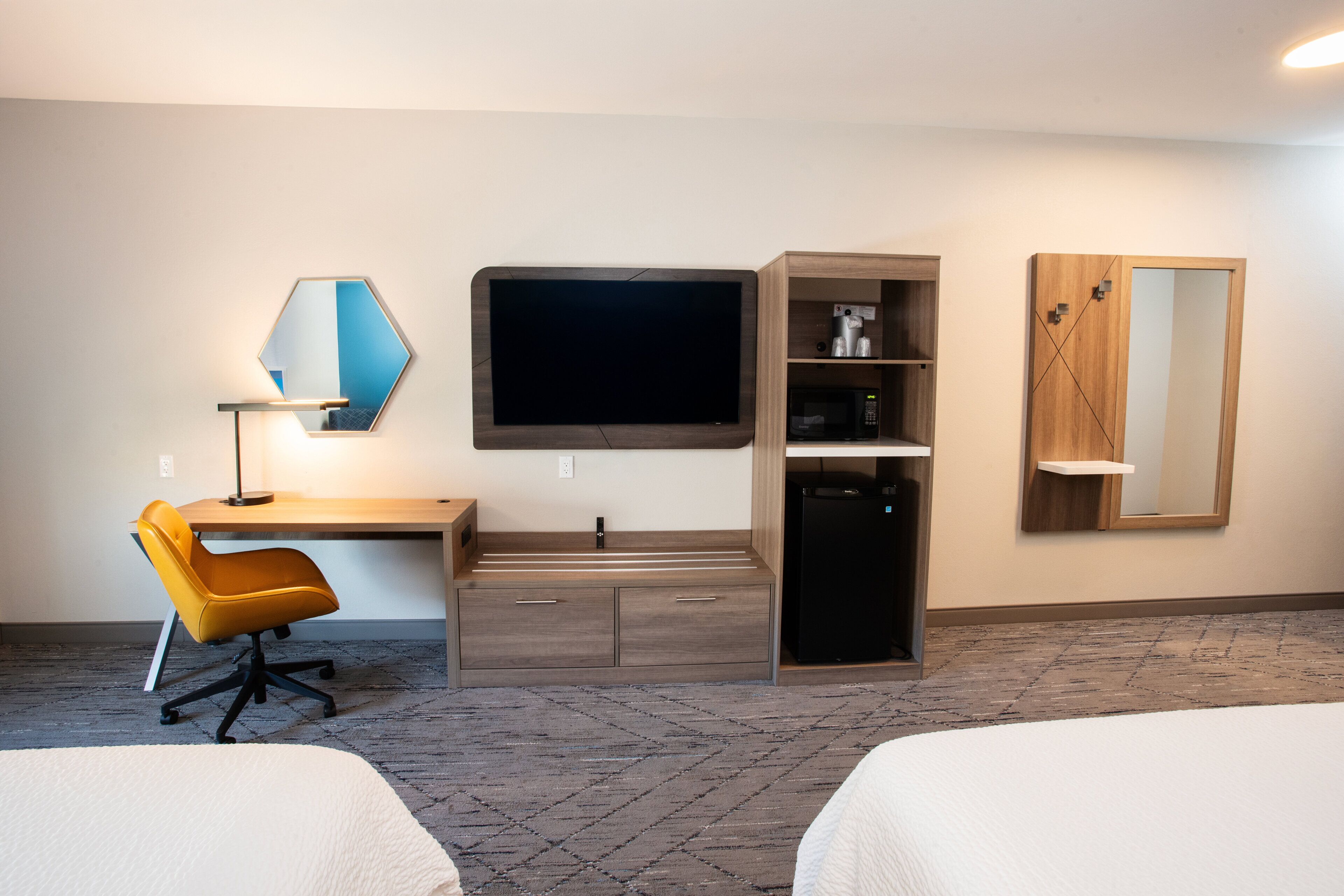 Une chambre d’hôtel équipée d’un bureau, d’une chaise, d’un lit, d’une télévision, d’un four à micro-ondes et d’une armoire.