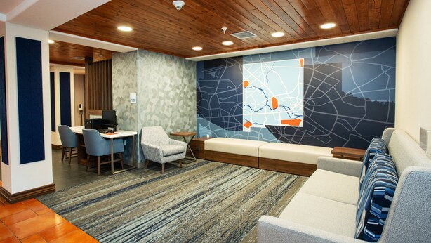 A modern hotel lobby with a wooden ceiling, a seating area with a sofa and chairs, a small table with a computer, and a decorative wall with a map design. - Holiday Inn Express & Suites Las Cruces North by IHG (Las Cruces)