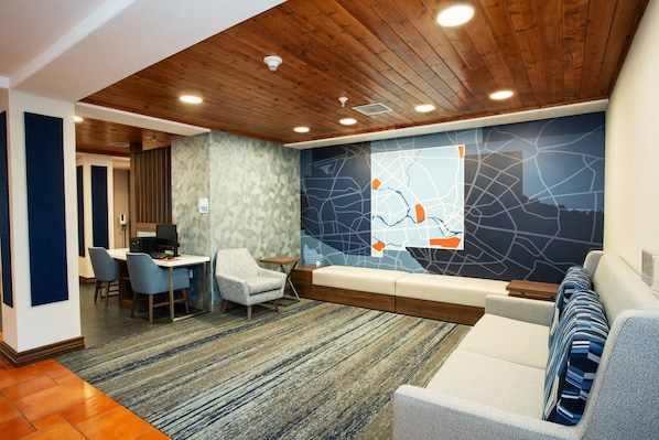 A modern hotel lobby with a wooden ceiling, a seating area with a sofa and chairs, a small table with a computer, and a decorative wall with a map design. - Holiday Inn Express & Suites Las Cruces North by IHG (Las Cruces)