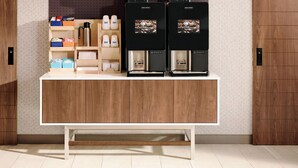 A coffee station with two coffee machines, a shelf with coffee cups, and a storage area with boxes and a thermos. - Holiday Inn Express & Suites Las Cruces North by IHG (Las Cruces)